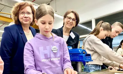 Staatssekretärin Dr. Ute Leidig (rechts) und VBK-Personalchefin Stephanie Schulze (links) schauen einer Teilnehmerin des Aktionstages im VBK-Betriebshof am Karlsruher Rheinhafen über die Schulter.