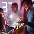 Zwei Männer und zwei Mädchen begutachten Elektronik in einem kleinen gelben Koffer. Im Hintergrund läuft ein Countdown.