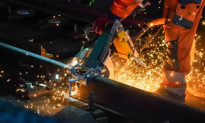 Das Symbolfoto zeigt nächtliche Gleisbauarbeiten an einer Bahnstrecke. Ein Mitarbeiter eines Bautrupps zertrennt Schienen mit einer Flex. Dabei sprühen Funken.
