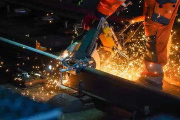 Das Symbolfoto zeigt nächtliche Gleisbauarbeiten an einer Bahnstrecke. Ein Mitarbeiter eines Bautrupps zertrennt Schienen mit einer Flex. Dabei sprühen Funken.