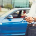 Ein Mann zeigt einen Autoschlüssel und deutet auf ein blaues Auto.