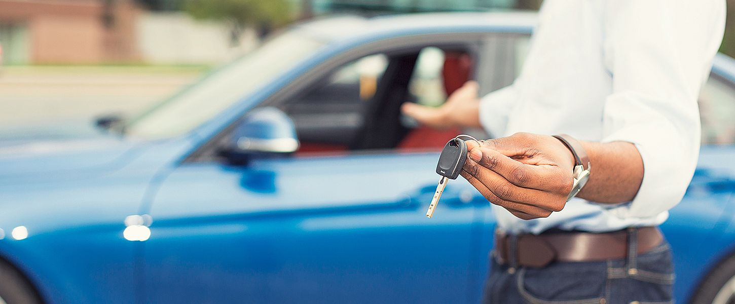 Ein Mann zeigt einen Autoschlüssel und deutet auf ein blaues Auto.