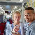 Eine junge Frau und ein junger Mann stehen mit Handy in der Bahn.