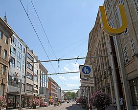 Die Kaiserstraße in Karlsruhe, eingerahmt von Häuserfassen. Der Himmel ist blau und die Sonne scheint.