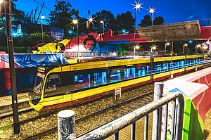 Eine AVG-Stadtbahn der Linie S1/S11 passiert nachts den Streckenabschnitt an der Haltestelle Kurt-Schumacher-Straße. Die Haltesstelle ist mit großflächigen Graffiti von Street-Art-Künstlern gestaltet.