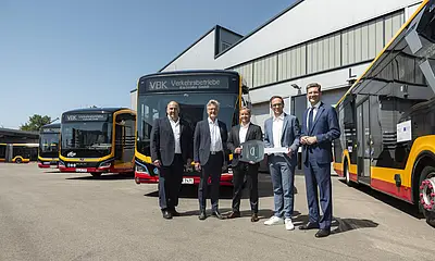 Vor E-Bussen steht eine Gruppe von Männern.