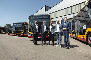Vor E-Bussen steht eine Gruppe von Männern.