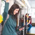 Eine Frau steht lächelnd in einer Bahn. Sie schaut auf ein Tablet in ihrer Hand.