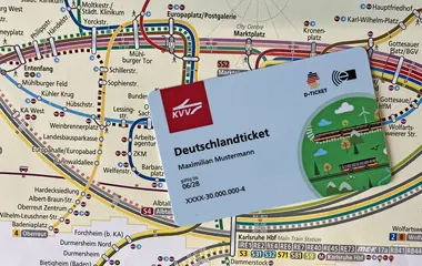 Das Foto zeigt das Deutschlandticket in Form einer Plastik-Karte. Im Hintergrund ist eine Liniennetzplan des Karlsruher Verkehrsverbundes abgebildet.  