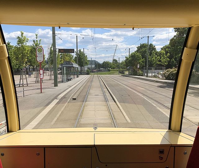 Aus der Frontscheibe der Fahrerkabine einer KVV-Bahn sieht man die zu diesem Zeitpunkt menschenleere Haltestelle Europahalle/Europabad bei sonnigem Wetter.