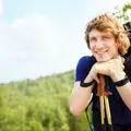 Ein Wanderer mit großem Rucksack stützt sich lächelnd auf seine Wanderstöcke.