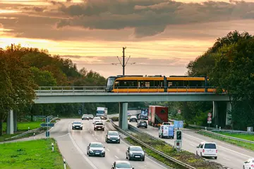 Eine Bahn der AVG überquert auf einer Brücke die Südtangente. Auf der Südtangente fahren Autos. Der Himmel ist bewölkt.