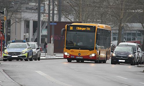 Ein gelber Bus der Linie 30 steht an einer Kreuzung. Links im Bild ist ein Polizeiauto zu sehen, rechts ein normaler PKW