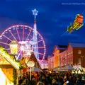 Weihnachtsmarkt Karlsruhe mit beleuchteten Gebäuden, Riesenrad und vielen Besuchern. Der fliegende Weihnachtmarkt fliegt mit seinen Rentieren über den weihnachtlich, geschmückten Platz. 
