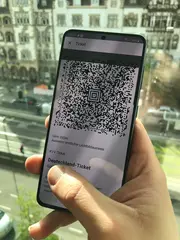 Eine Hand hält ein Smartphone. Auf dem Display ist ein QC-Code bzw. das Deutschland-Ticket zu sehen.