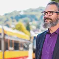 Ein Mann mittleren Alters mit Brille und Bart wartet an einer Bahn-Haltestelle.