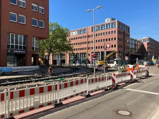Das Foto zeigt die aktuellen Gleisbauarbeiten am Kronenplatz im Kruzungsbereich Kaiserstraße/Fritz-Erler-Straße. Zu sehen sind Bagger, Baumaschinen und Absperrbarken sowie Gebäudefassaden im Bildhintergrund.