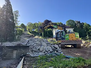 Das Foto zeigt des Rückbau der alten Talstation der Turmbergbahn. Ein gelber Bagger schaufelt Betonreste zur Seite.