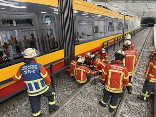 Mehrere Feuerwehrleute stehen neben einer Bahn. Sie versuchen während eine Übung die Bahn mit technischem Werkzeug zu heben. 