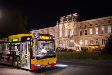Ein Bus der KAMUNA-Ringbuslinie 1 hält nachts vor dem Naturkundemuseum, dessen Fassade von Scheinwerfern angestrahlt wird.