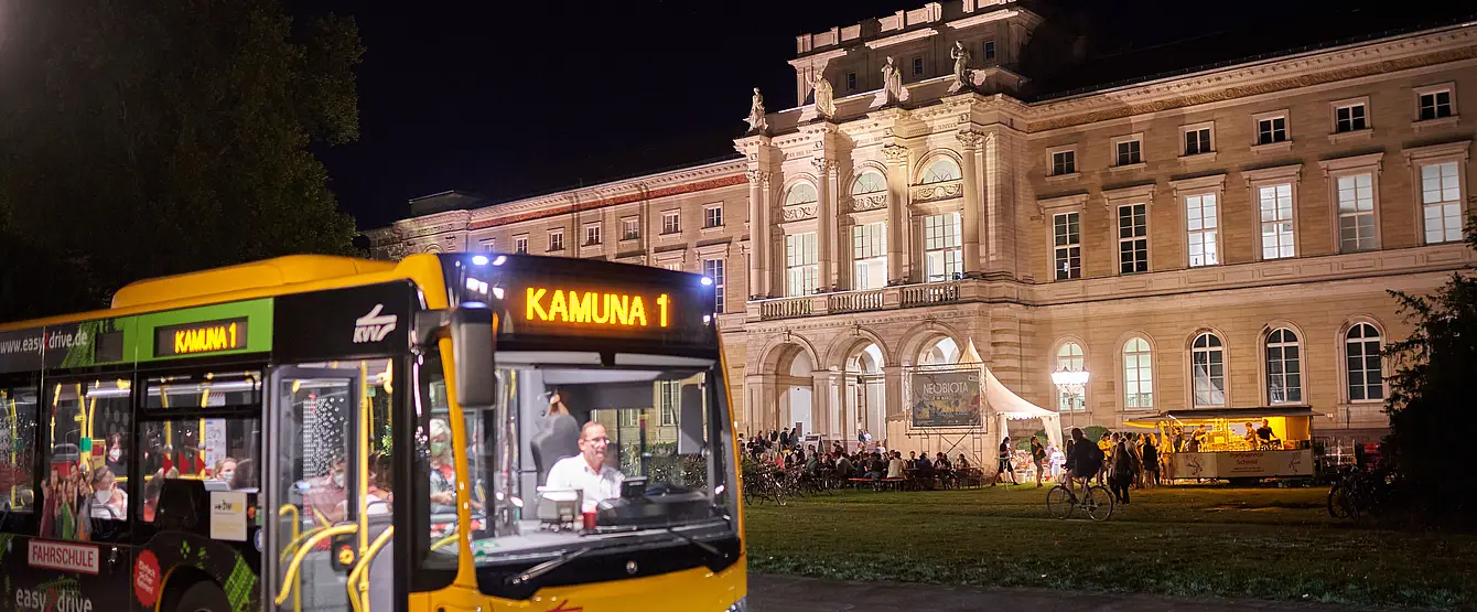 Ein beleuchteter VBK-Bus steht vor dem beleuchteten Naturkundemuseum in Karlsruhe. 