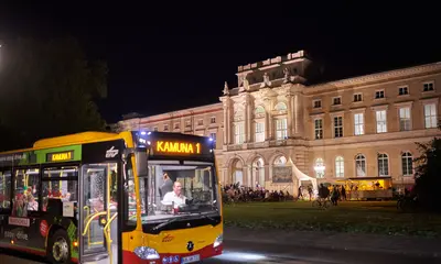 Ein Bus der KAMUNA-Ringbuslinie 1 hält nachts vor dem Naturkundemuseum, dessen Fassade von Scheinwerfern angestrahlt wird.
