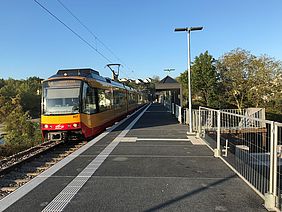 Der neue Bahnsteig am Schulzentrum Bretten und eine einfahrende Stadtbahn der AVG vor blauem Himmel