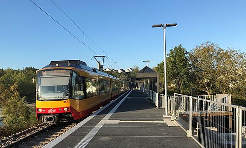 Der neue Bahnsteig am Schulzentrum Bretten und eine einfahrende Stadtbahn der AVG vor blauem Himmel