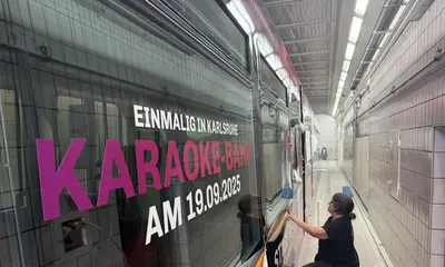 Eine Frau foliert im Betriebshof West im Lackierraum eine VBK-Bahn mit dem Schriftzug: "Einmalig in Karlsruhe. Karaoke-Bahn am 19. September 2025".