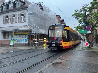 Eine VBK-Trambahn fährt durch die Pfinztalstraße in Durlach. Im Hintergrund ist ein Haus mit einem Baugerüst zu sehen.