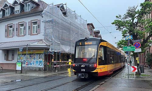 Eine VBK-Trambahn fährt durch die Pfinztalstraße in Durlach. Im Hintergrund ist ein Haus mit einem Baugerüst zu sehen.
