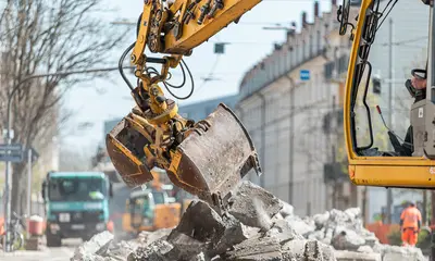 Das Symbolfoto zeigt eine Baumaßnahme in Karlsruhe. Ein gelber Bagger hebt herausgebrochene Asphaltstücke an.