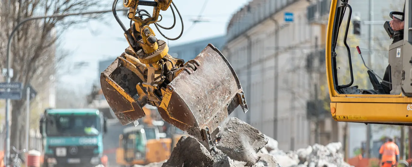 Das Symbolfoto zeigt eine Baumaßnahme in Karlsruhe. Ein gelber Bagger hebt herausgebrochene Asphaltstücke an.