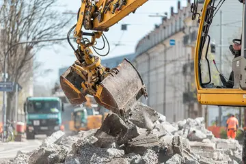 Das Symbolfoto zeigt eine Baumaßnahme in Karlsruhe. Ein gelber Bagger hebt herausgebrochene Asphaltstücke an.