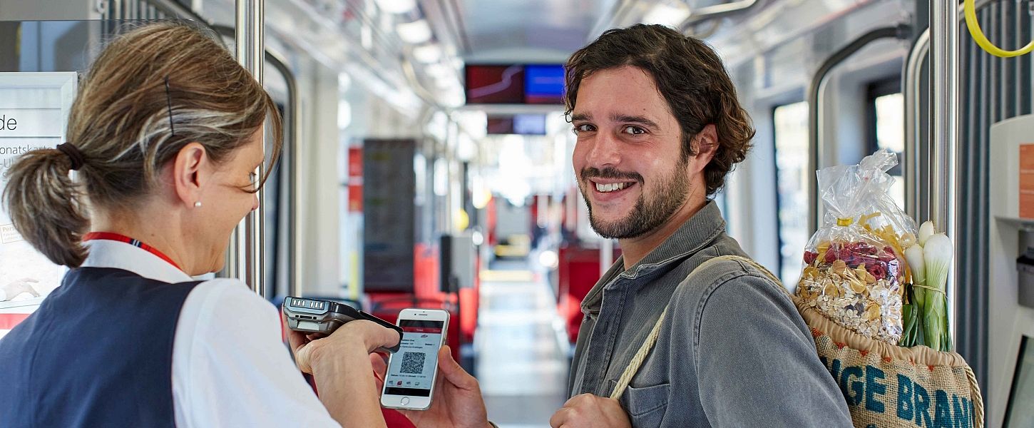 Mann zeigt einer Kontrolleurin seine Fahrkarte auf dem Smartphone.