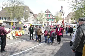 Das Symbolfoto zeigt Passanten und Teilnehmer*innen des Oster- und Higgo-Marktes in Heidelsheim. Am Straßenrand stehen Verkaufsstände. Im Hintergrund sind Häuser und ein Kirchturm zu sehen. 