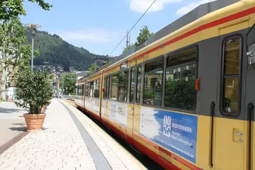 Seitenansicht einer AVG-Stadtbahn in der Innenstadt von Bad Wildbad vor hellblauem Himmel.