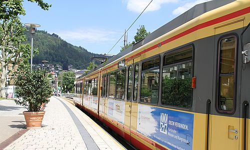 Seitenansicht einer AVG-Stadtbahn in der Innenstadt von Bad Wildbad vor hellblauem Himmel.