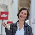 Eine Frau mit einem Schlüssel in der Hand steht lächelnd vor einem KVV-Kundenzentrum.
