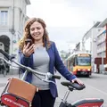 Frau mit Fahrrad schauta auf ihr Smartphone. Im Hintergrund sind Bahnen zu sehen.