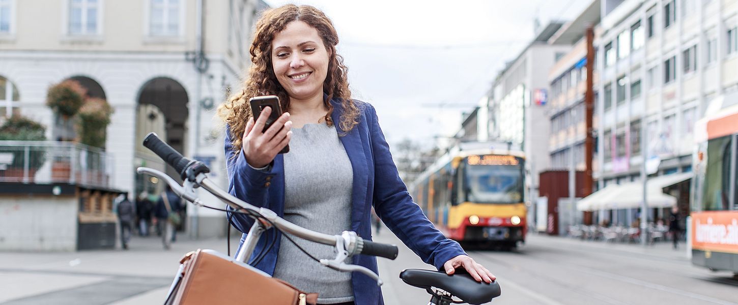 Frau mit Fahrrad schauta auf ihr Smartphone. Im Hintergrund sind Bahnen zu sehen.