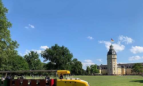 Eine gelbe Schlossgartenbahn vor dem Karlsruher Schloss und hellblauem Himmel
