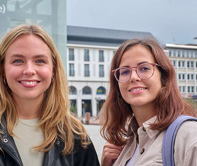 Zwei junge Frauen stehen auf dem Karlsruher Marktplatz und lächeln.