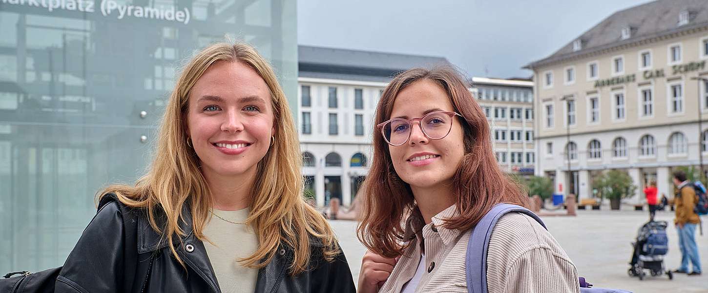 Zwei junge Frauen stehen auf dem Karlsruher Marktplatz und lächeln.