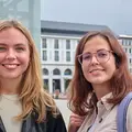 Zwei junge Frauen stehen auf dem Karlsruher Marktplatz und lächeln.