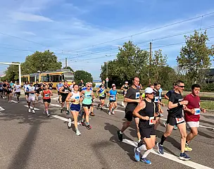 Teilnehmer*innen des Baden-Marathons in Karlsruhe laufen entlang der Durlacher Allee. Im Hintergrund fährt eine Bahn vorbei.