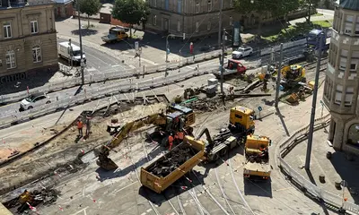 Blick von oben auf die Baustelle am Gleisviereck Tullastraße. Es sind ein gelber Bagger und ein gelber Lastwagen zu sehen.