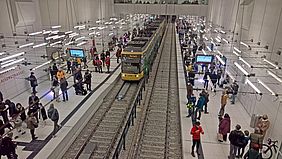 Haltestelle im Stadtbahntunnel mit Passagieren an den Bahnsteigen und einer einfahrenden Bahn.