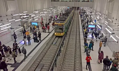 Haltestelle im Stadtbahntunnel mit Passagieren an den Bahnsteigen und einer einfahrenden Bahn.