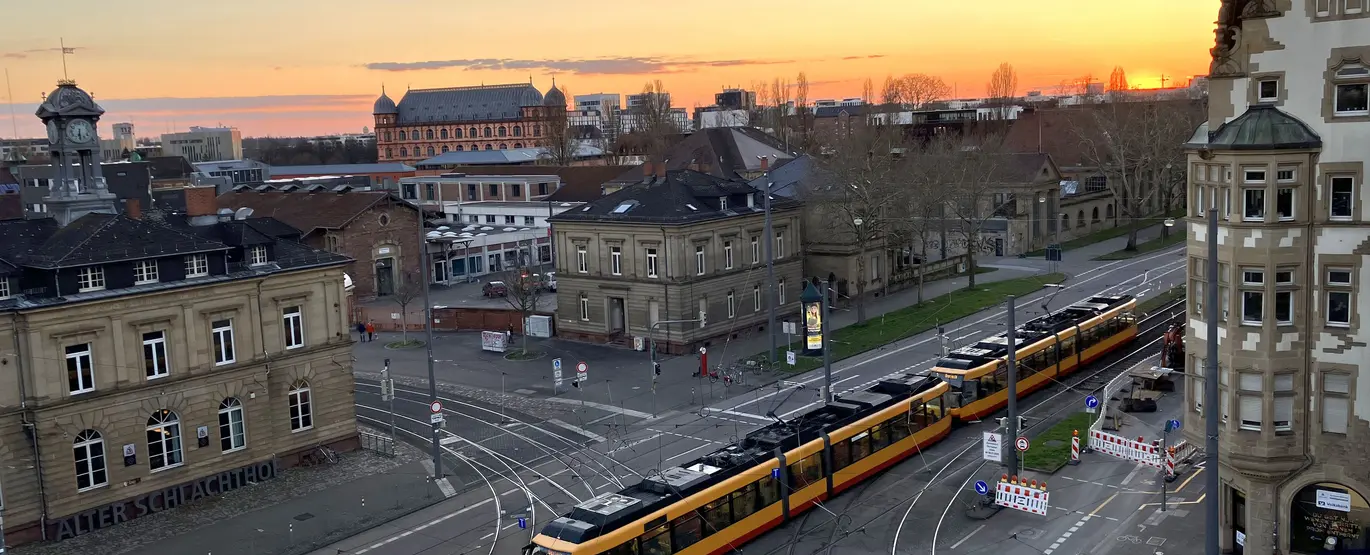 Blick von oben auf das Gleisviereck Schlachthof, Durlacher Allee und Tullastraße von schräg oben. Die untergehende Abendsonne taucht das Bild in eine dunkel-orangefarbene Lichtstimmung. 
